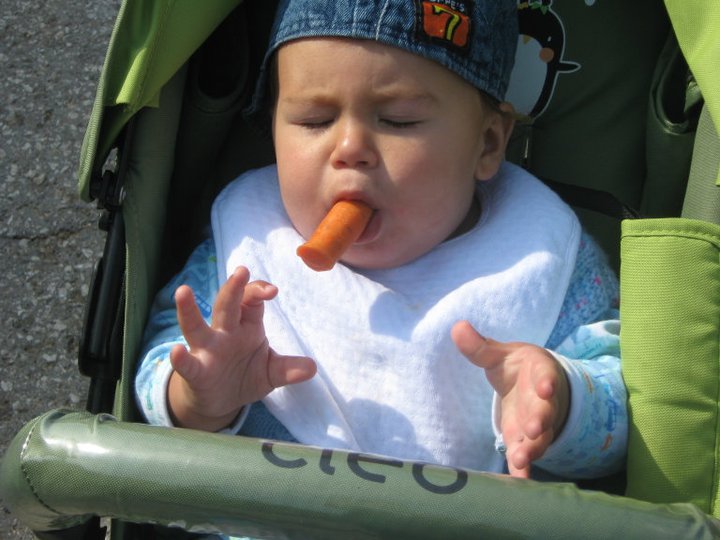 Малко дете се опитва да яде морков докато се вози на детска количка